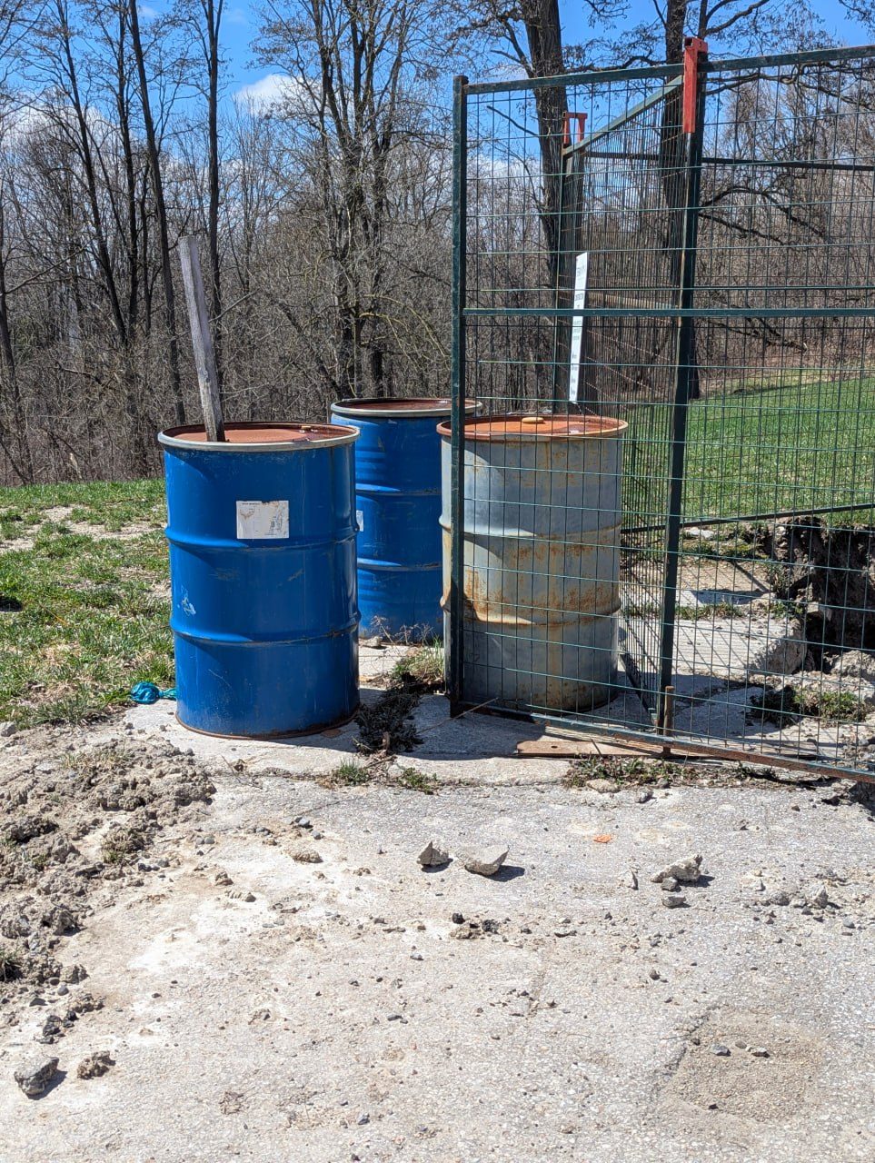 Soil drums staged at a fenced, wooded remediation site